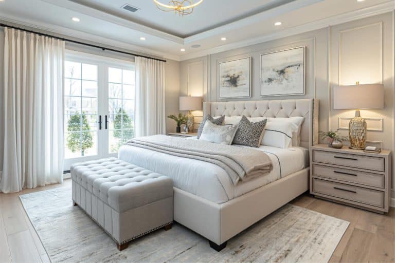 Elegant bedroom with large bed, upholstered bench, bedside tables with lamps, and wall art. Doors open to a patio. Enjoy the ultimate comfort with our premium mattresses & sleep essentials.