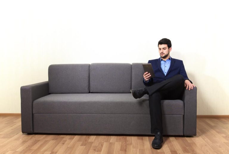 A businessman sitting on a black formal sofa, holding a tablet.