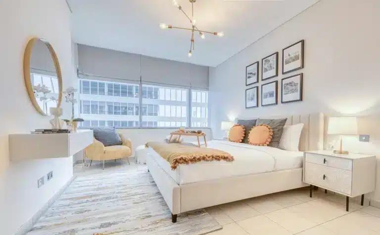 white bedroom with bed, ottoman, side table and armchair