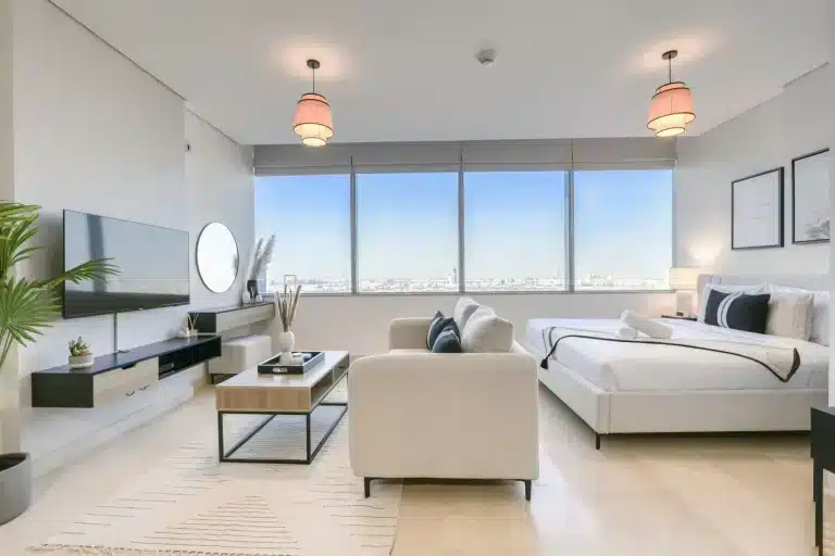 Modern hotel room with a large bed, wall-mounted TV, beige sofa, and a coffee table.