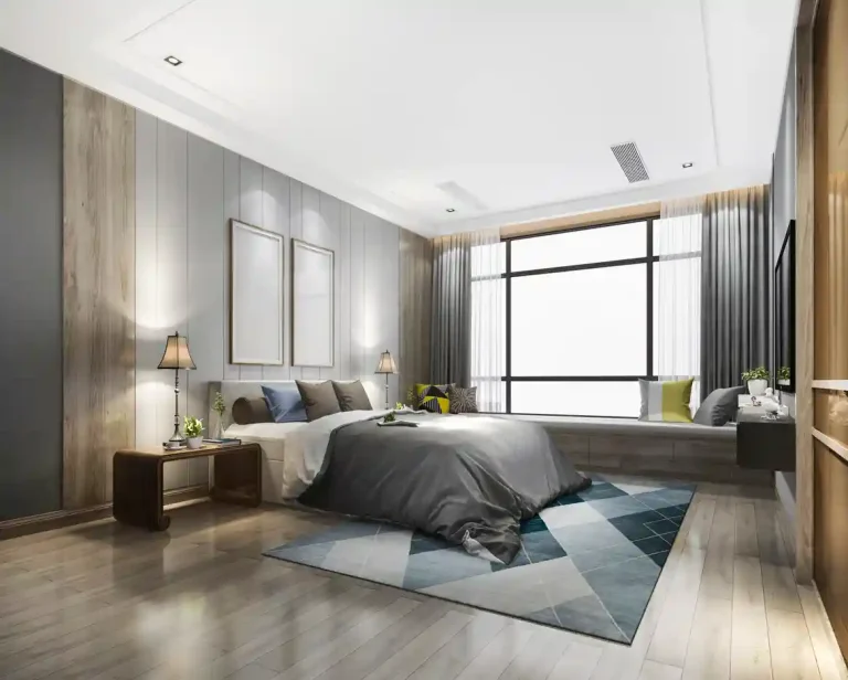 Modern bedroom with a large bed, gray bedding, two bedside lamps, and a window seat. Walls feature wood paneling, and the floor has a geometric-patterned rug.