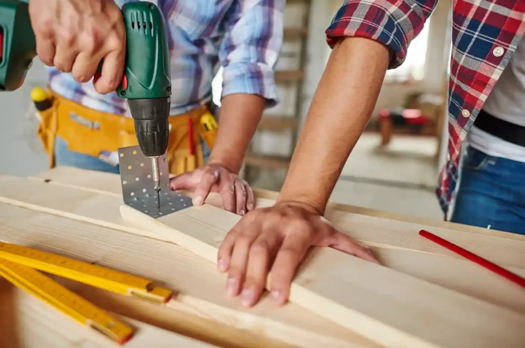 Two people engaged in a customized project at a wooden table, utilizing a drill for bespoke shape modifications.