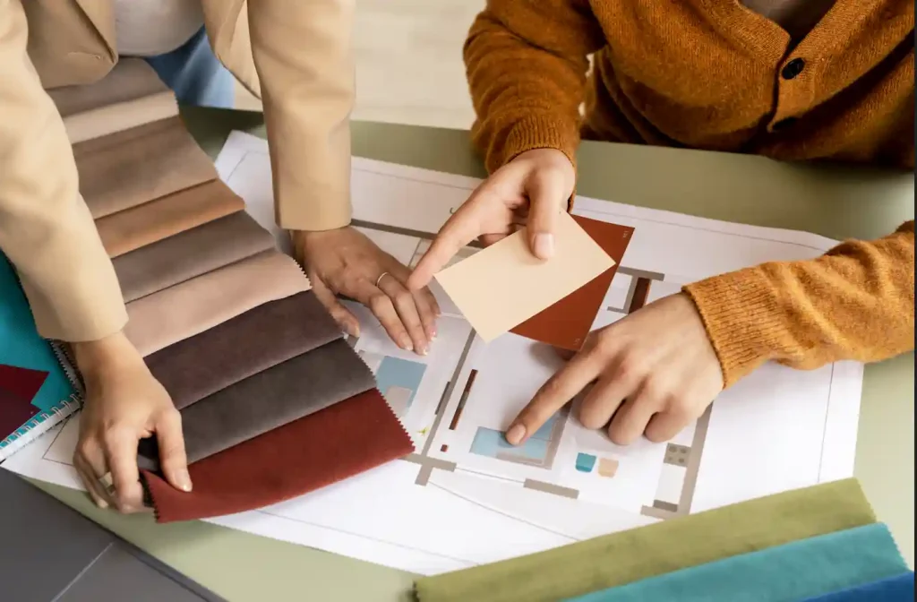 Two individuals examining various fabric samples spread out on a table, engaged in discussion about their choices.