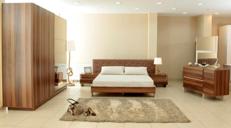 A cozy bedroom featuring a neatly made bed, a wooden dresser, and a large mirror reflecting the room's decor.