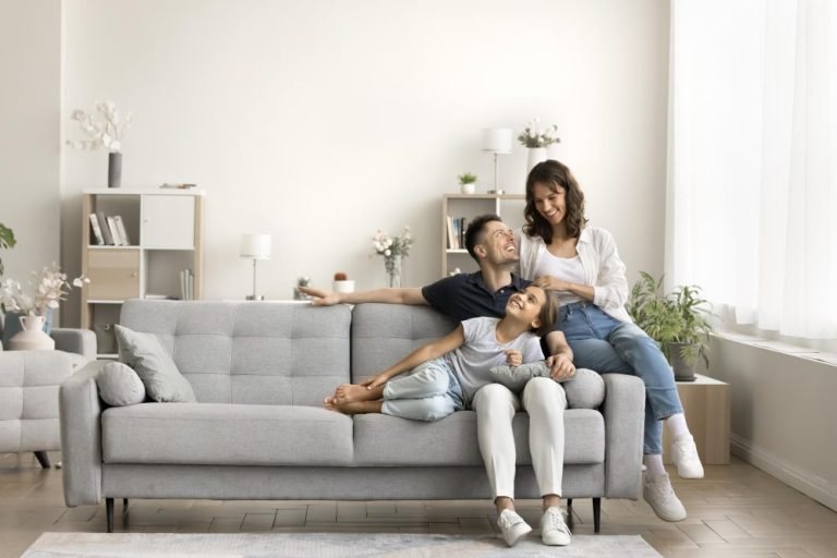 A family of four sitting together on a couch in a cozy living room, smiling and enjoying each other's company.